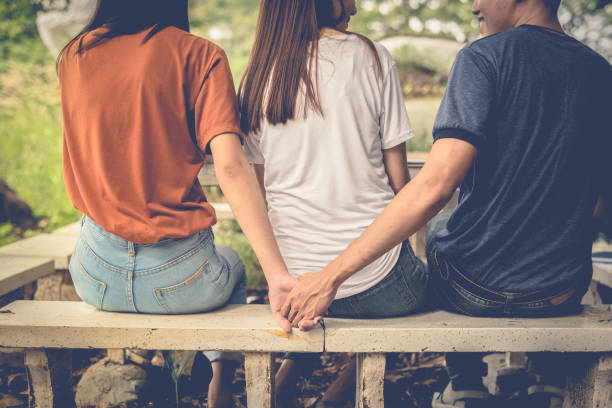 Boyfriend and another woman grab hands from behind together without sight of his girlfriend.. Paramour and divorce concept. Social problem and cheating couples theme. Teen adult and University theme. stock photo