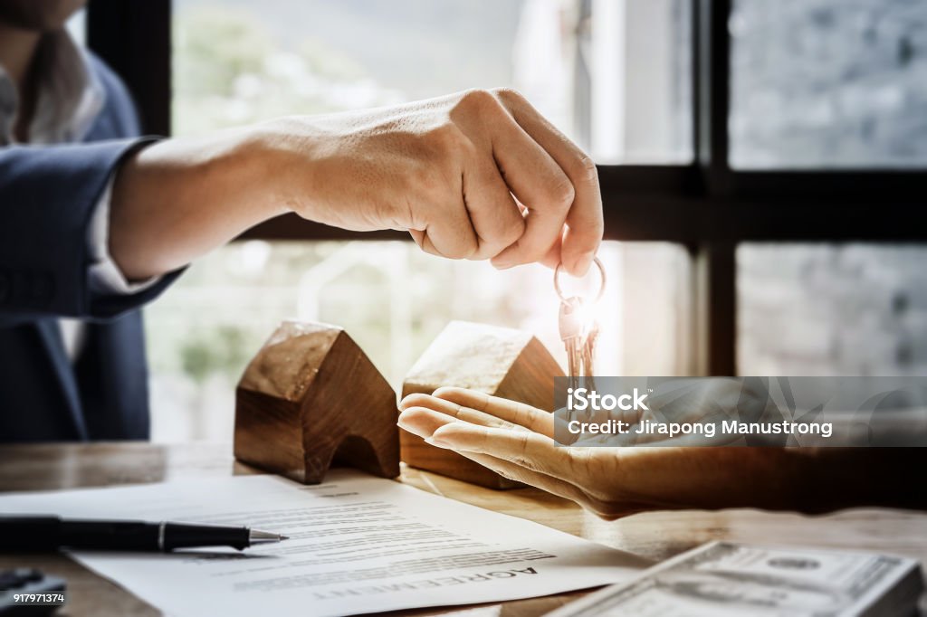 estate agent giving house keys  of customer  and holding dollar us bank at  agency office. agreement concept. Real Estate Stock Photo