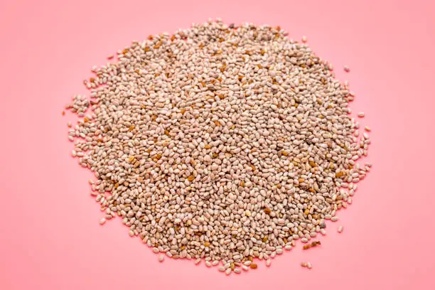 a small pile  of organic white chia seeds rich in omega-3 fatty acids, top view on a pink background