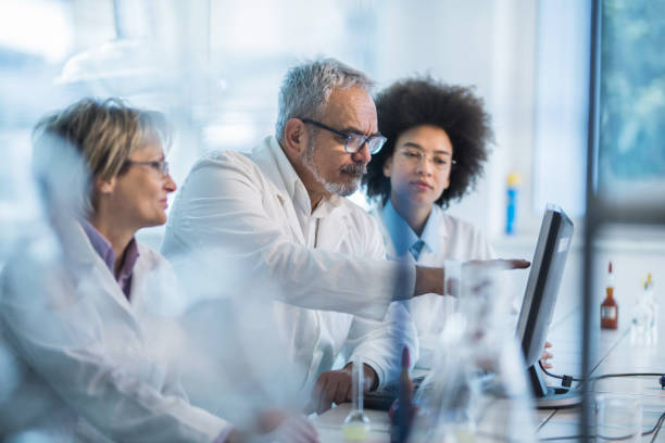 Team of biotechnologists working on desktop PC in laboratory. Group of doctors analyzing medical data on a computer in the laboratory. Focus is on man aiming at computer monitor. researcher and doctor stock pictures, royalty-free photos & images