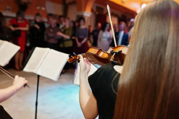 Photo of Close-up portrait of a beautiful young female violinist playing violin on the wedding in restaurant.
