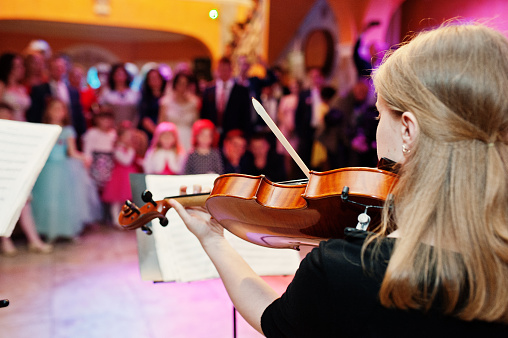 Close-up portrait of a beautiful young female violinist playing violin on the wedding in restaurant.
