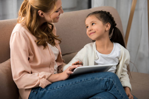 istock happy mother and daughter smiling each other while using digital tablet at home 918031810