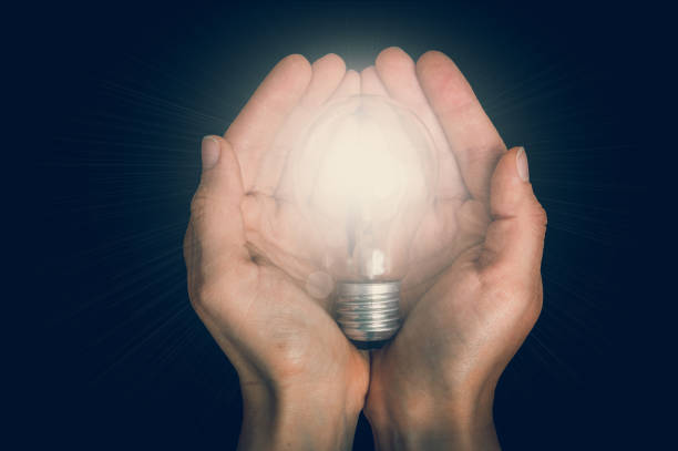 istock Glowing light bulb in female hands isolated on black 918039288