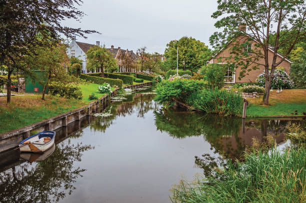 istock Charming small canal next to rustic houses with lush gardens and trees reflected on the water in cloudy day at Drimmelen. 918039366