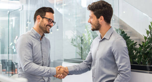 istock Two smiling businessmen shaking hands together while standing in modern office. 918045902
