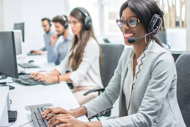 Photo of Smiling young woman with headset working in call center.