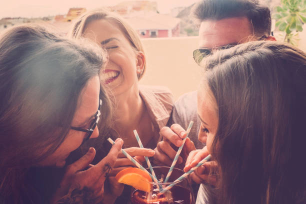 2 couples of guys drink a red drink on the terrace with 4 blue and white straws. All neighbors laughing pass a fun free time. Vintage filter