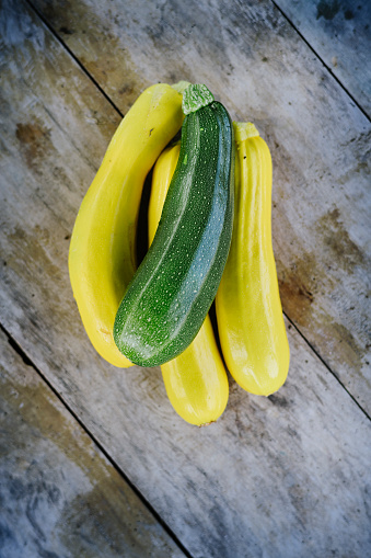 Overhead view of a selection of freshly picked, organically grown courgettes. Vertical, photographed from above on a rustic wooden background.