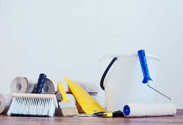 istock Composition with various tools for wallpapering and rolls of wallpaper against white empty wall 918090688