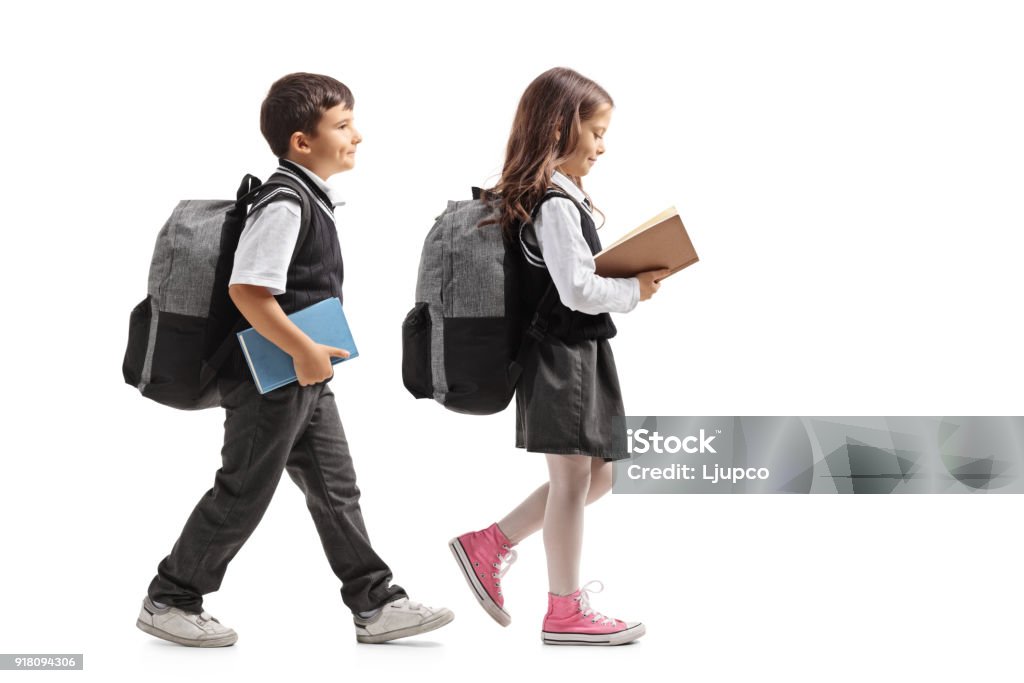 Full length profile shot a schoolboy and a schoolgirl with backpacks and books walking Full length profile shot a schoolboy and a schoolgirl with backpacks and books walking isolated on white background Child Stock Photo