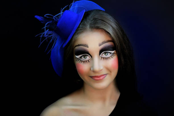 Beautiful girl with creative make-up for the Halloween party. Bright colors faceart, pink lips, stylish hair dress design. Conceptual art broken porcelain doll with big cracks on the cheeks, forehead