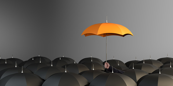 Business Man holding orange colored umbrella between the black umbrellas