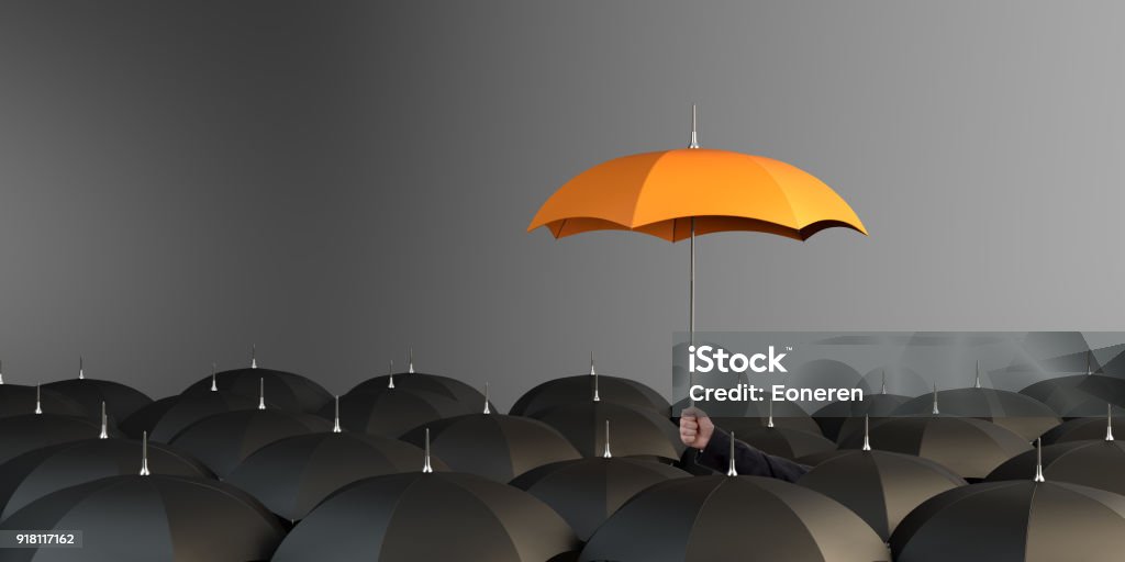 Orange Colored Umbrella Between The Black Umbrellas Business Man holding orange colored umbrella between the black umbrellas Insurance Stock Photo