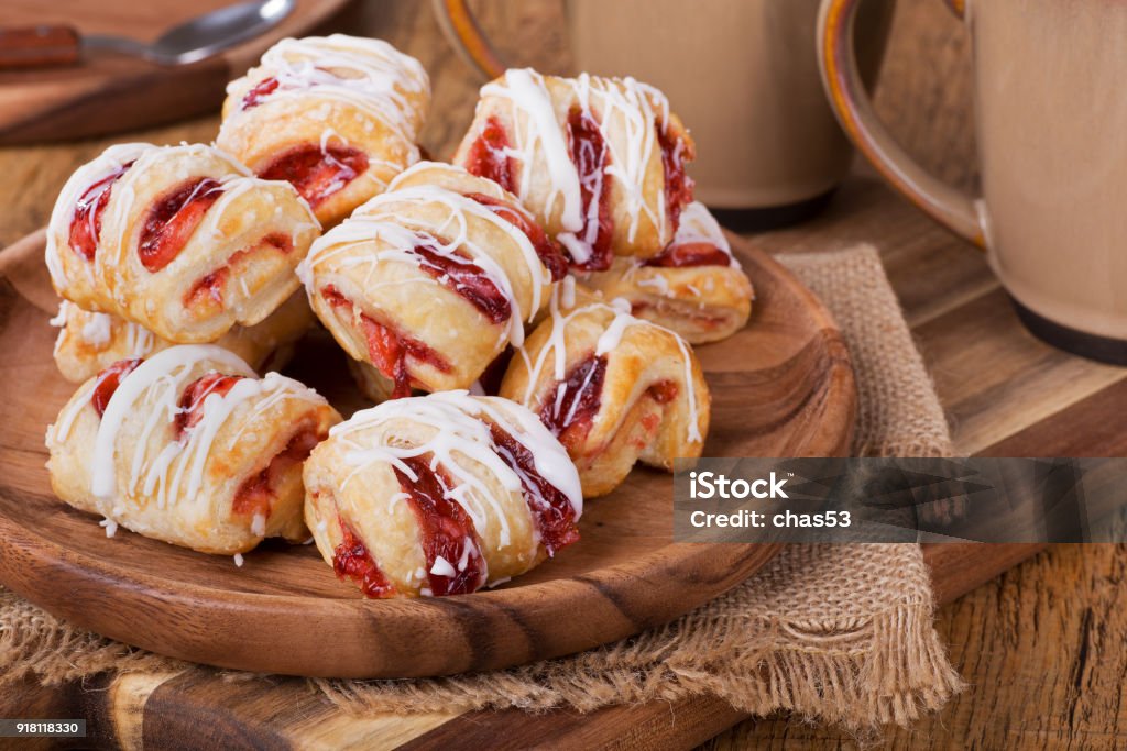 Strawberry Pastry Sweets Pile of strawberry pastries on a wooden plate with coffee mugs in background Strudel Stock Photo