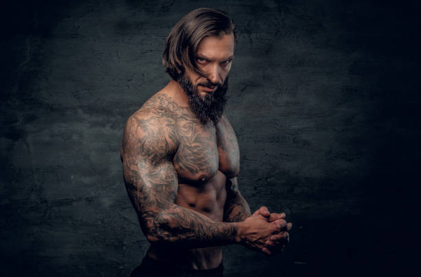 Portrait of a  man with tattooed body. Studio portrait of bearded man with shirtless, tattooed body on grey background. cross shoulder tattoos stock pictures, royalty-free photos & images
