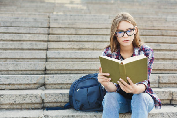 istock Young woman reading book on university stairs 918123946