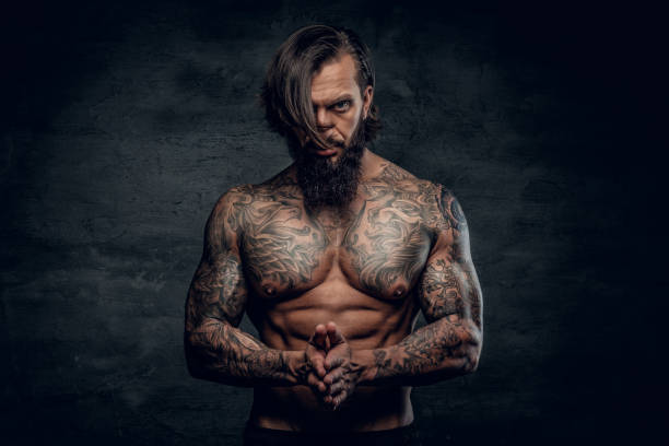 Portrait of a  man with tattooed body. Studio portrait of bearded man with shirtless, tattooed body on grey background. shoulder tattoo designs for men stock pictures, royalty-free photos & images