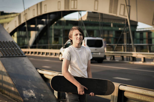 Teenage boy holding skateboard across his shoulder. Low angle view.