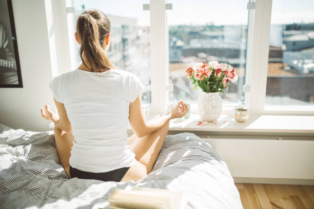 Beautiful woman practicing yoga in front of window of cozy apartment.Relaxation and mindfulness concept. stock photo
