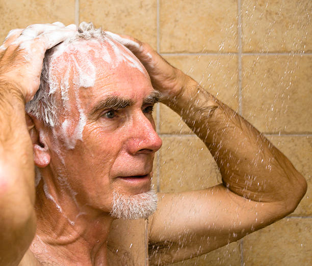 Senior man washing hair in shower stock photo