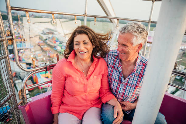 Active Senior Couple at the Fairground Active senior visit the fairground to enjoy the rides together ferris wheel stock pictures, royalty-free photos & images