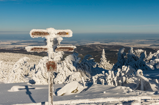 Sign for hiking in winter on the mountain Brocken with heavy snow covered firs in the sunshine.