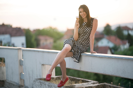 Portrait of a beautiful, young woman  wearing dotted dress, sitting on the balcony fence and eating ice cream.
