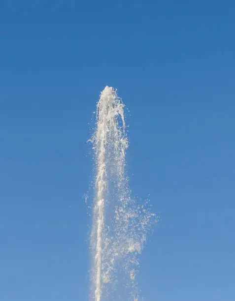 Photo of a large stream of pure water gushes up under pressure on the background of blue sky