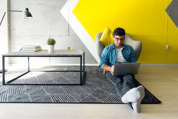 Freelancer Casually dressed guy working in simple and modern space. Dominant color of the space is yellow. small office interior stock pictures, royalty-free photos & images