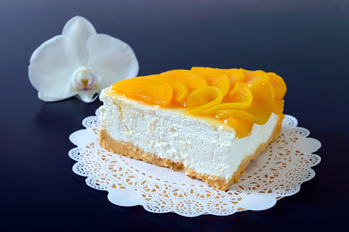 Delicate souffle with juicy peaches. A large delicious piece of cake on a golden stand on a black background.
