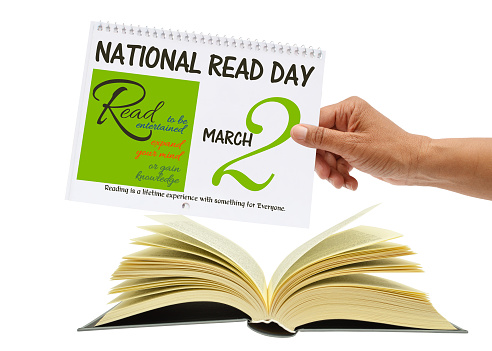 Hand holding National Read Day Calendar (Read to be entertained, expand your mind or gain knowledge) Reading is a lifetime experience with something for Everyone over opened book white background
