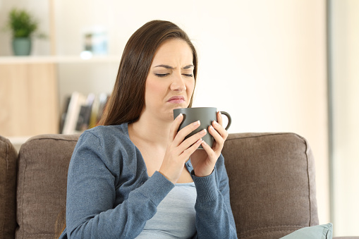 Woman suffering drink bad taste sitting on a couch in the living room at home