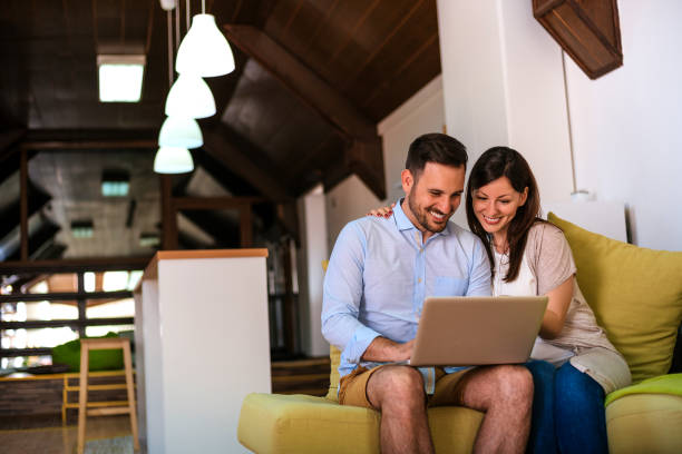 istock Image of happy boyfriend and girlfriend sitting on sofa while using laptop. 918170410
