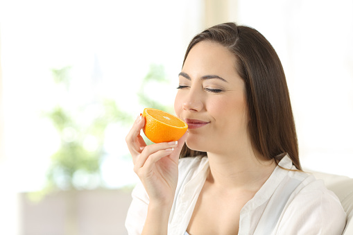 A young blond woman holds orange halves in her hands in the kitchen next to a table with fruits. The concept of diet, healthy eating.