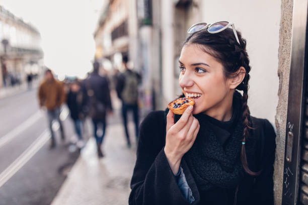 European tourist woman trying out local food.Eating traditional Portuguese egg custard tart pastry dessert pastel de Nata. stock photo