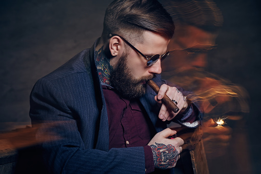 Tattooed bearded man in sunglasses smoking a cigar.