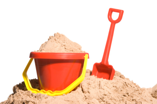 Picture of an Asian girl's hand in a swimsuit. Sitting in a pile of sand by the sea Using a toy sand scoop to scoop up wet sand.