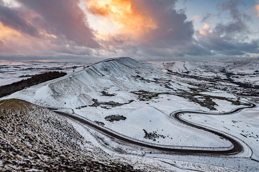 Winding road leading through English countryside covered in snow and dramatic sky.