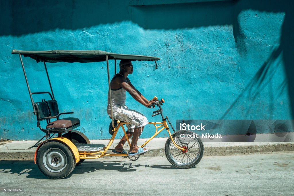 Bicycle taxi driver with his vehicle, Cuba Cuba taxi driver with his vehicle in front of blue wall Cuba Stock Photo