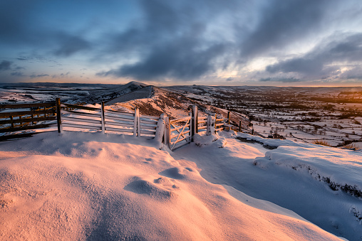 Fresh layer of snow with pink morning light and dramatic clouds at Mam Tor in the Peak District.