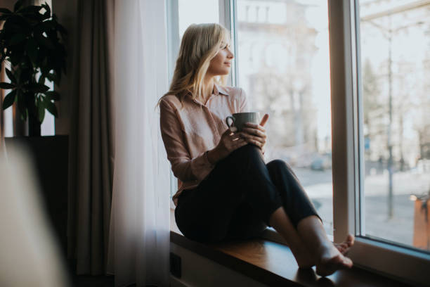 istock Blonde young woman drinking coffee by window 918201584