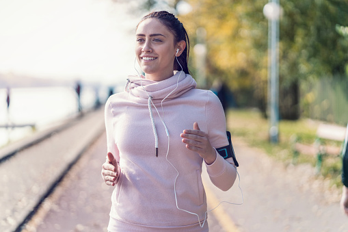 Close-up image of young cheerful woman listening to music while jogging in the park
