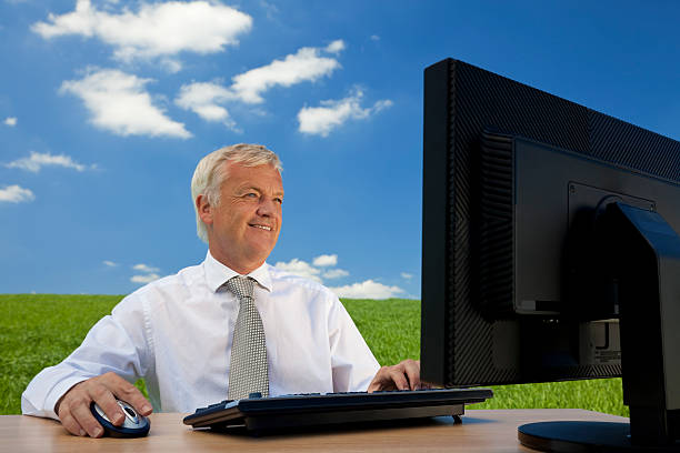 Blue Sky Thinking Business concept shot showing an older male executive using a computer in a green field with a blue sky complete with fluffy white clouds. Shot on location not in a studio. environment computer cloud leadership stock pictures, royalty-free photos & images