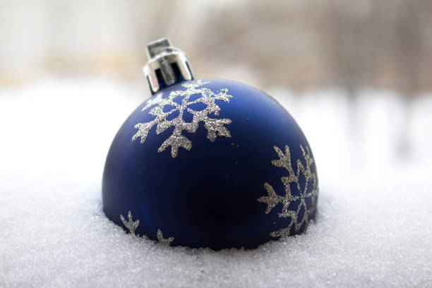 A large, shiny blue ball lies in the snow.  Toy, decoration for a house and a Christmas tree, close-up