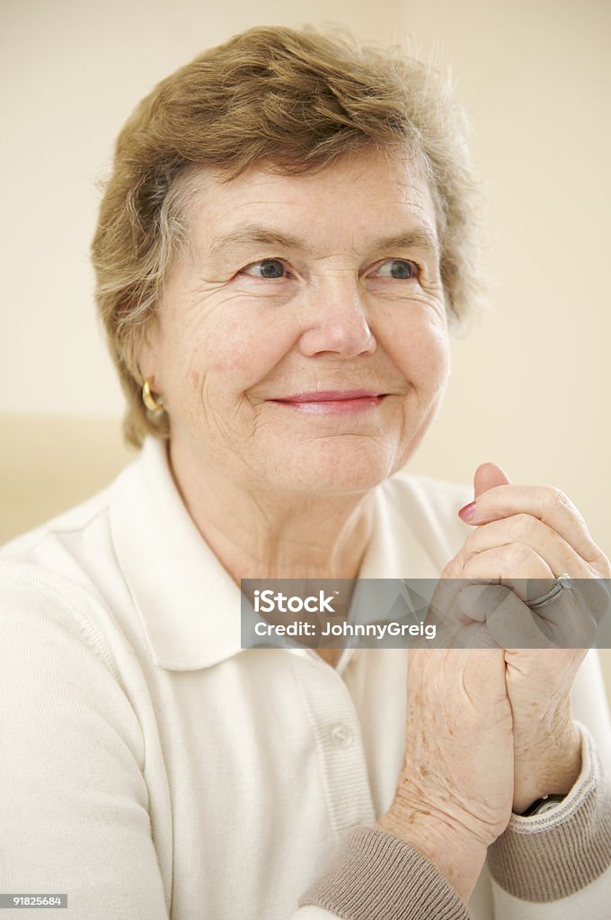 Smiling Female Senior Citizen with Hands Clasped in Joy  Beige Stock Photo