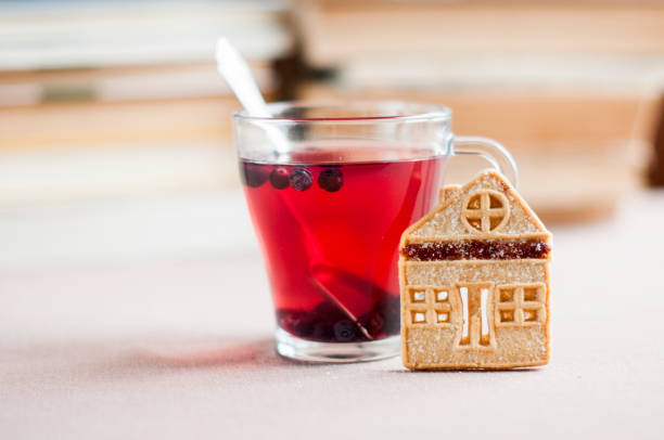 chá de mirtilo em uma tigela de vidro com bolinhos de shortbread sob a forma de uma casa no contexto dos livros - zeaxanthin - fotografias e filmes do acervo