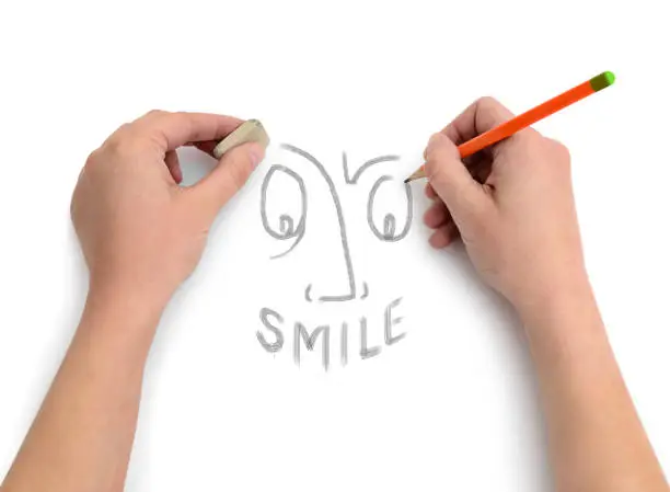 Hands of an artist draw a smile on white paper.