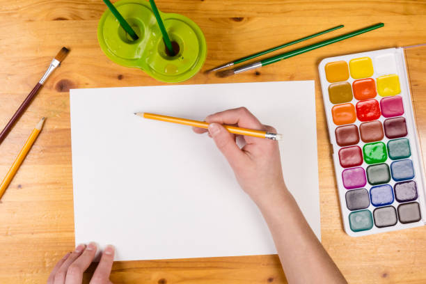 istock kids hand holding a pencil on blank page, top view 918304382