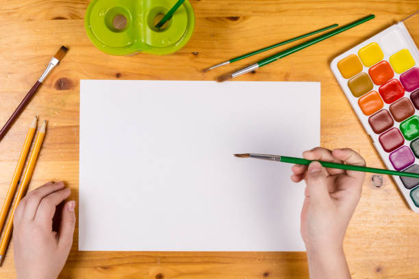 istock kids hand holding a paintbrush on blank page, top view 918304408